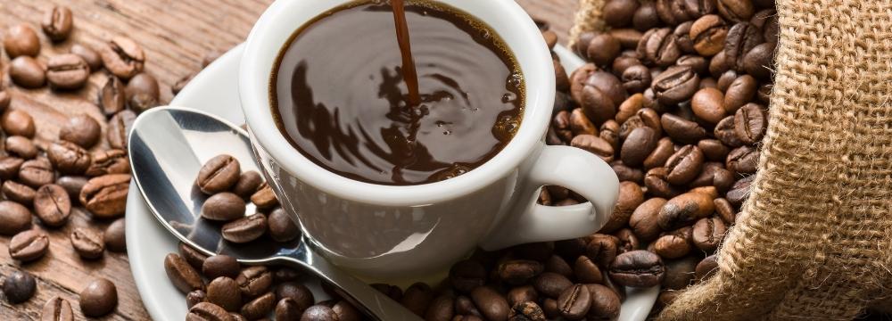 Coffee being poured into a mug on small plate with spoon, coffee beans scattered around mug and on wooden table